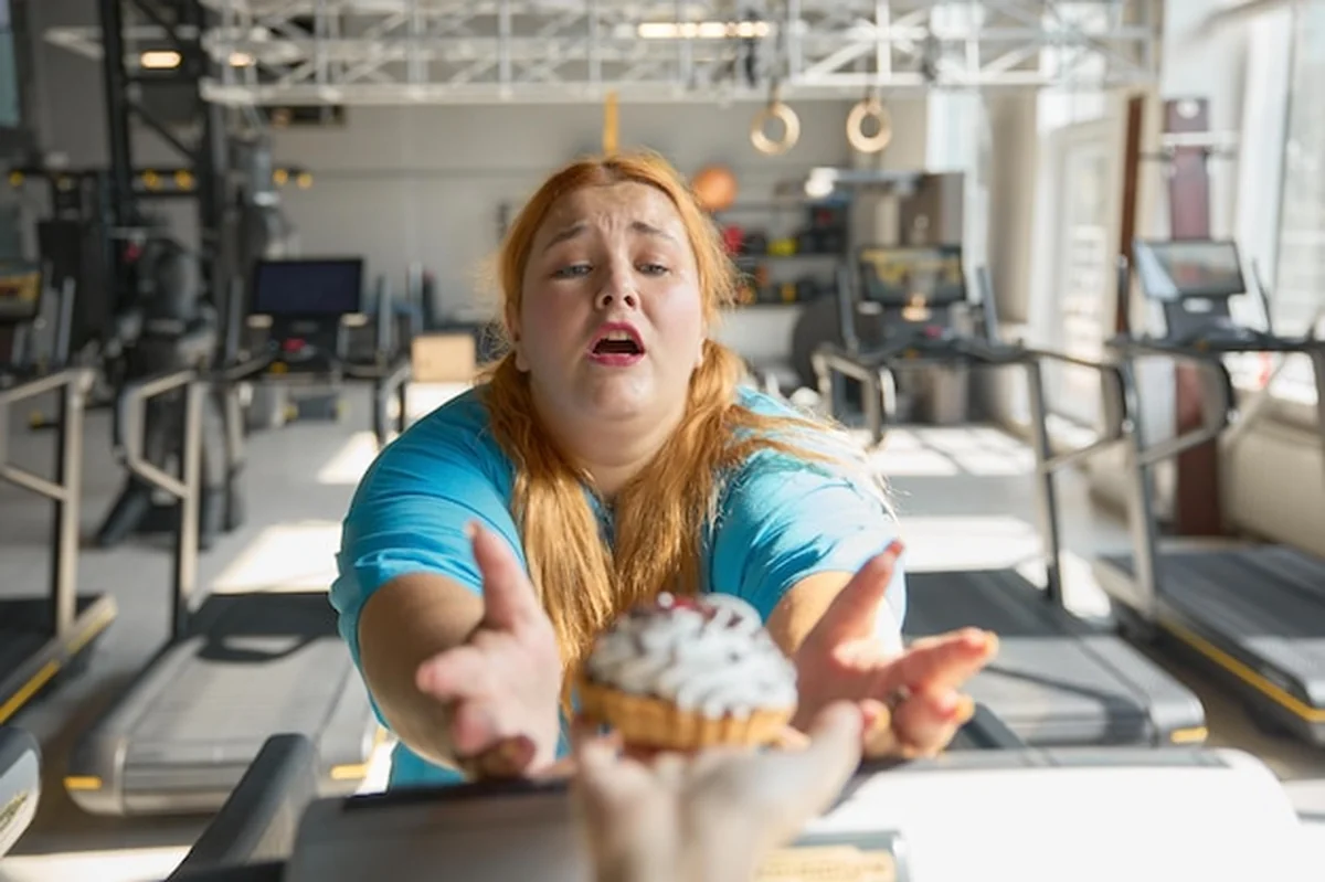 Otyła kobieta w siłowni sięgająca po ciasto
