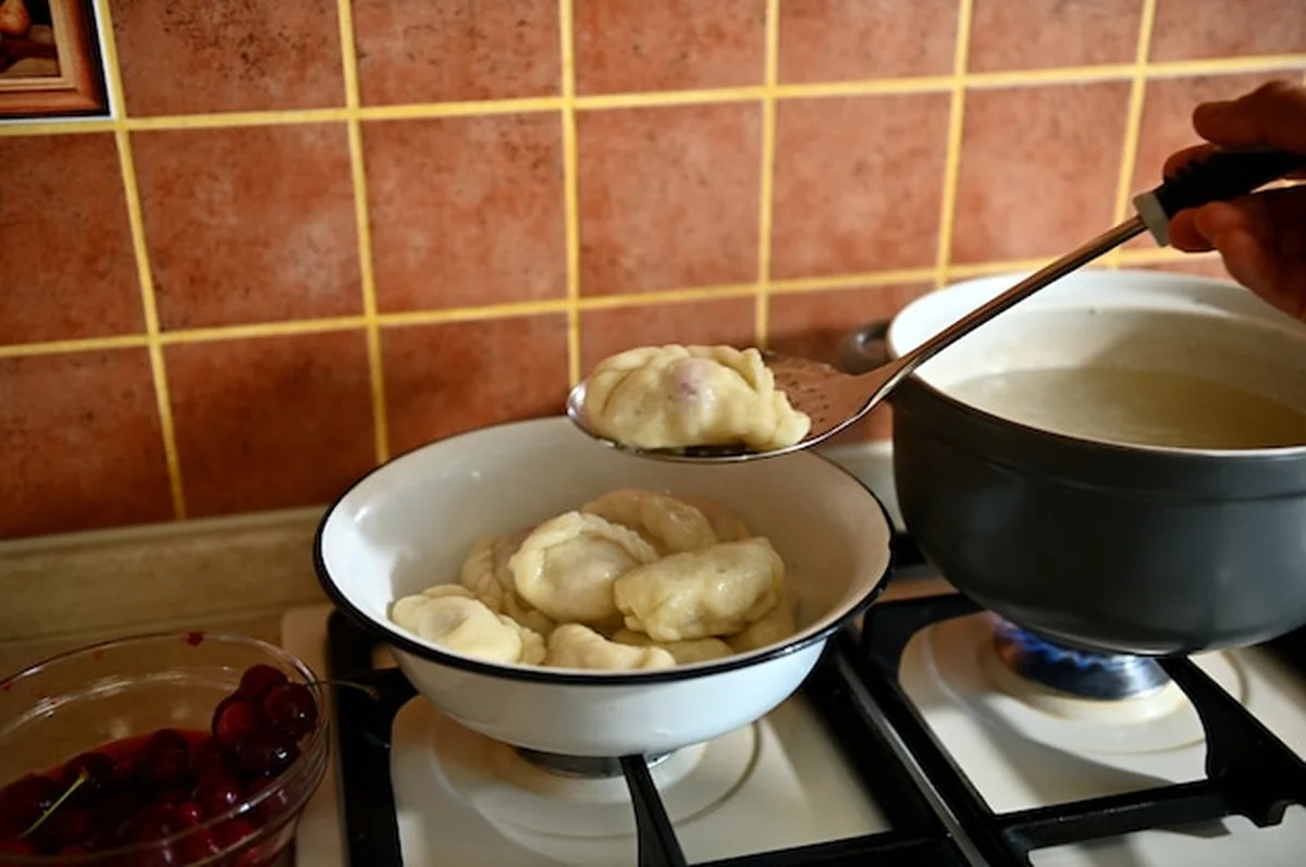 Cukiernik wyjmuje ugotowane knedle z wrzącej wody na durszlak