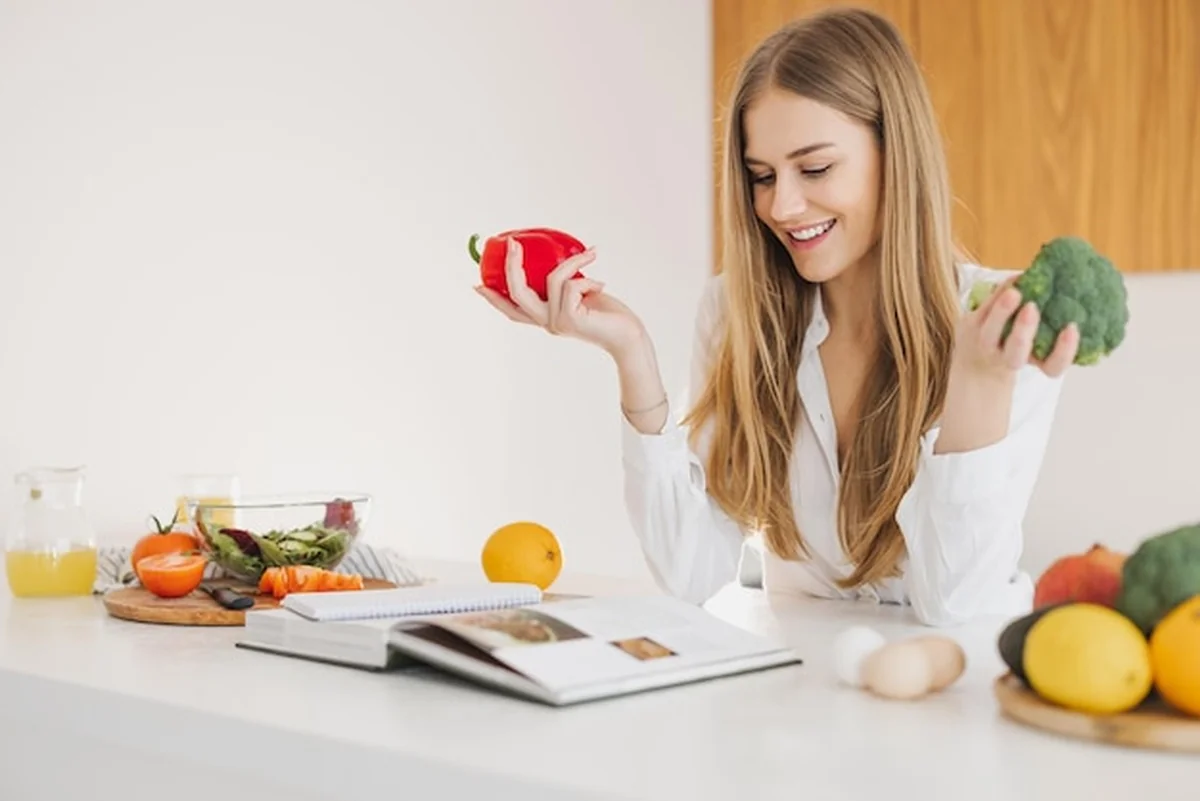 Blondynka trzymająca paprykę i brokuły, czytająca książkę z przepisami