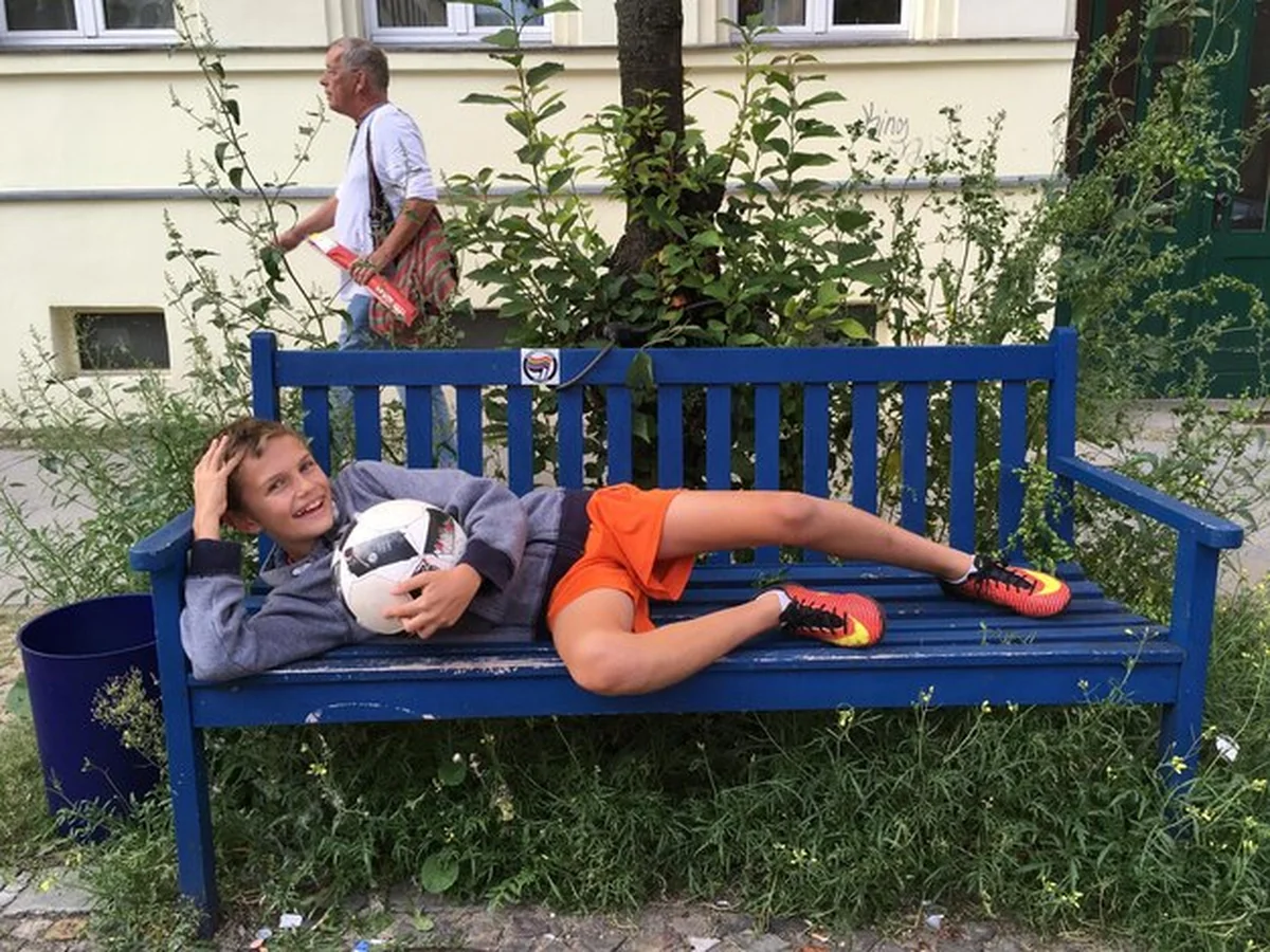 Uśmiechnięty chłopiec z piłką na ławce w parku