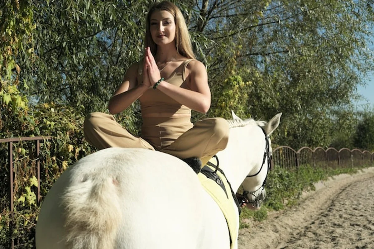 Blondynka w lekkich ubraniach ćwiczy gimnastykę na białym koniu