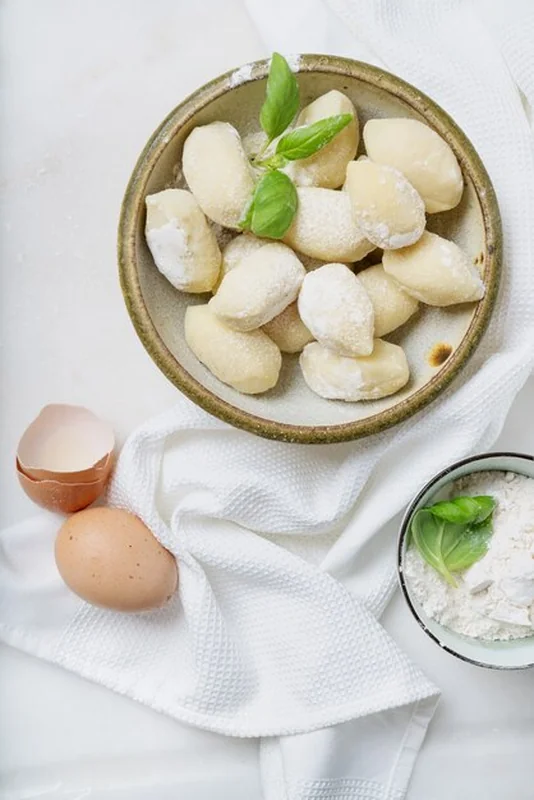 Tradycyjne włoskie gnocci ziemniaczane udekorowane bazylią, jajkami i mąką, widok z góry