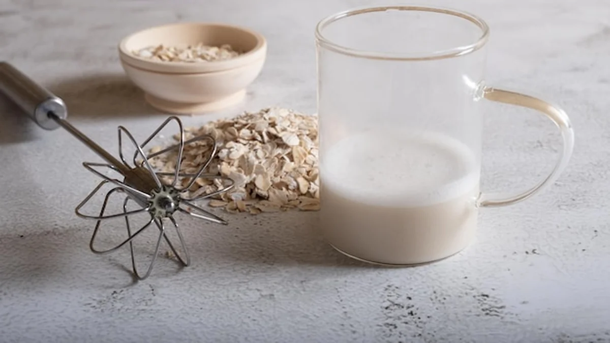 Ubite mleko owsiane w szklance i płatki owsiane na jasnym tle