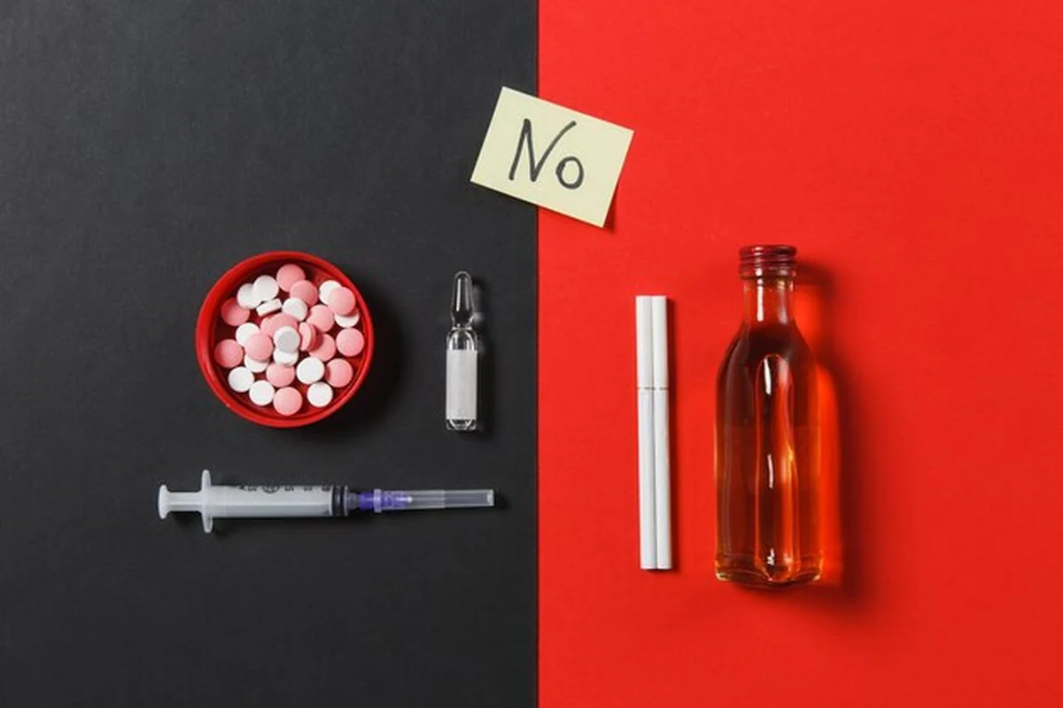 Kolorowe tabletki, pusta igła, butelka alkoholu, ampułka, papierosy