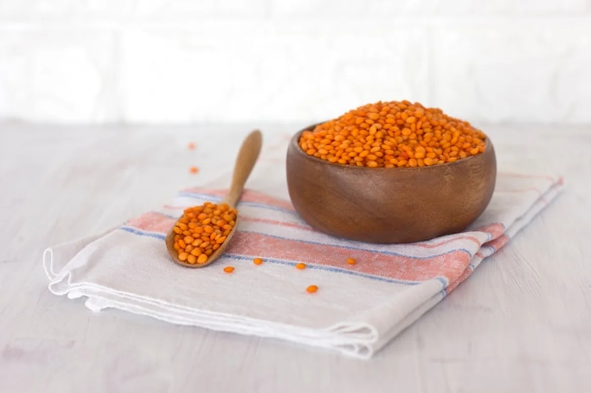 Surowe czerwone soczewicy w drewnianym pucharze i łyżce na bieliźnianej pielusze na białym stole