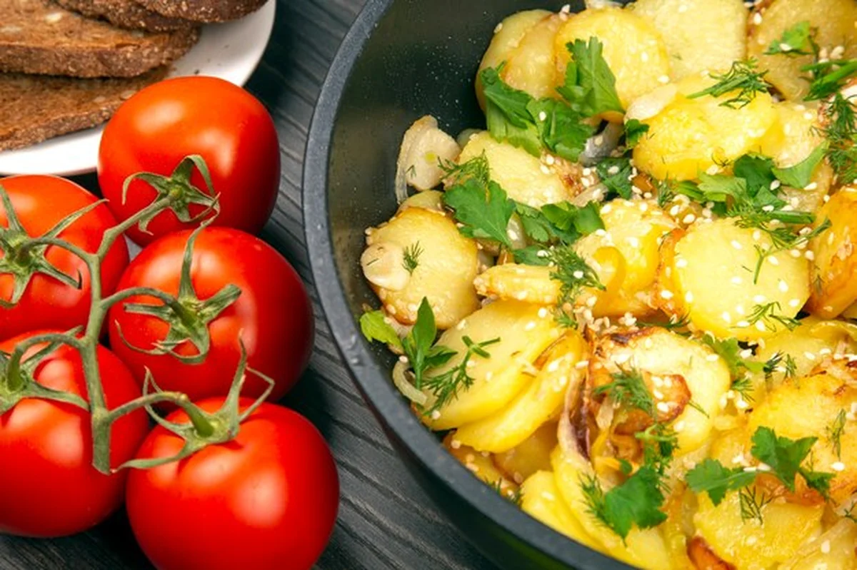 Gotowane smażone ziemniaki z ziołami, przyprawami i warzywami na czarnej patelni na drewnianym stole