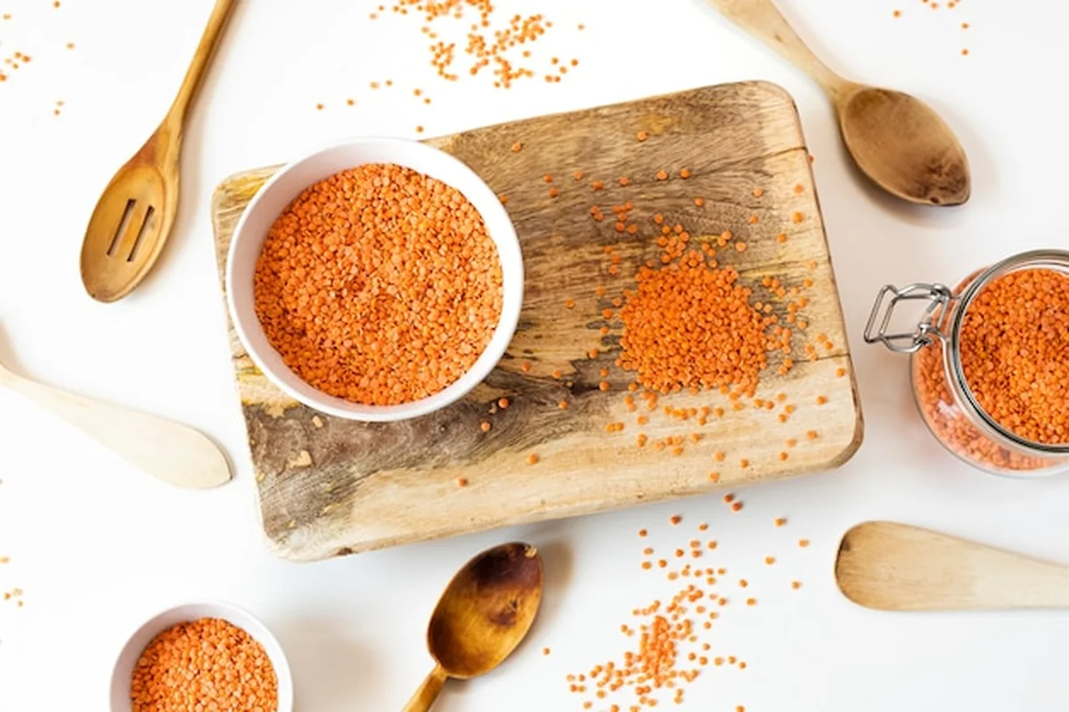 Martwa natura z czerwonej soczewicy w białej misce na drewnie z białym tłem z drewnianymi łyżkami