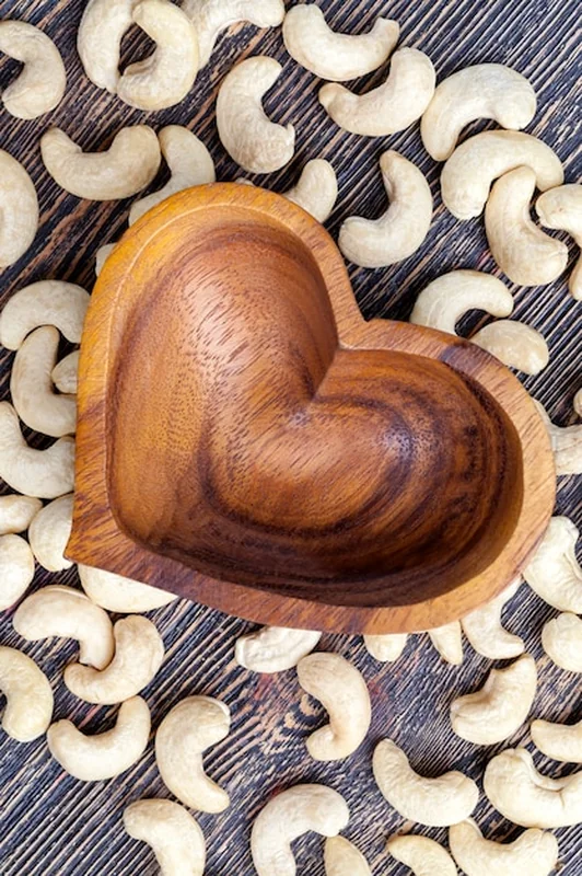 Surowe orzechy nerkowca obok miski w kształcie serca