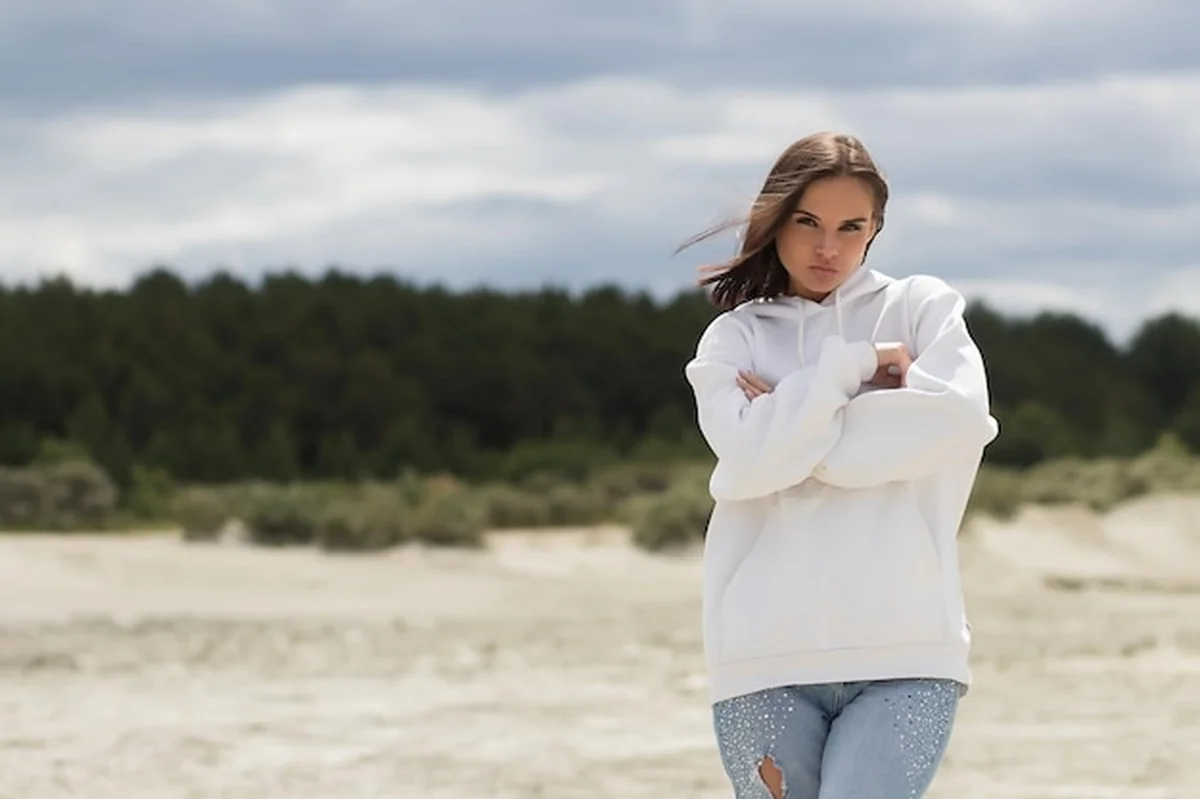 Młoda kobieta na plaży w luźnej bluzie, dotykająca brzucha w wietrzny dzień