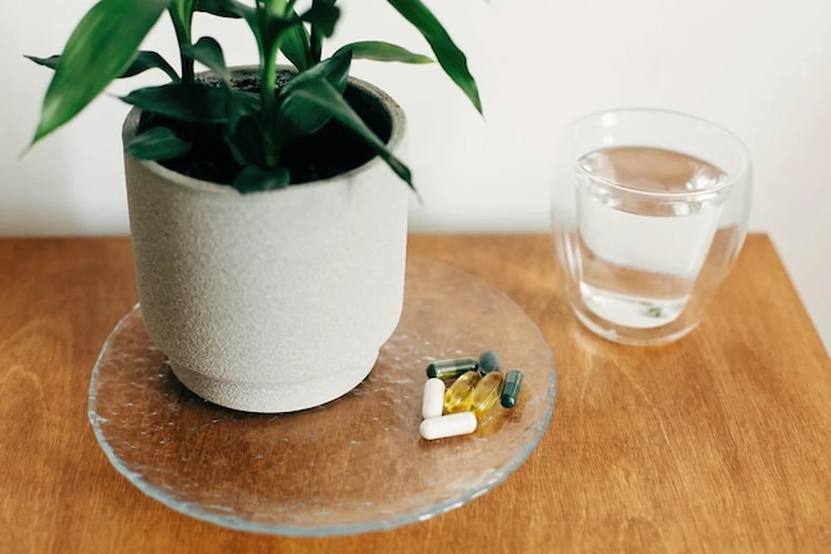 Suplementy diety na drewnianym stole - kapsułki Omega 3, spirulina, chlorofil, magnez i szklanka wody