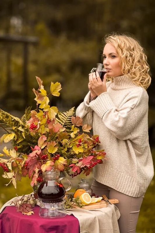 Dziewczyna pije herbatę wśród jesiennych liści obok jeziora